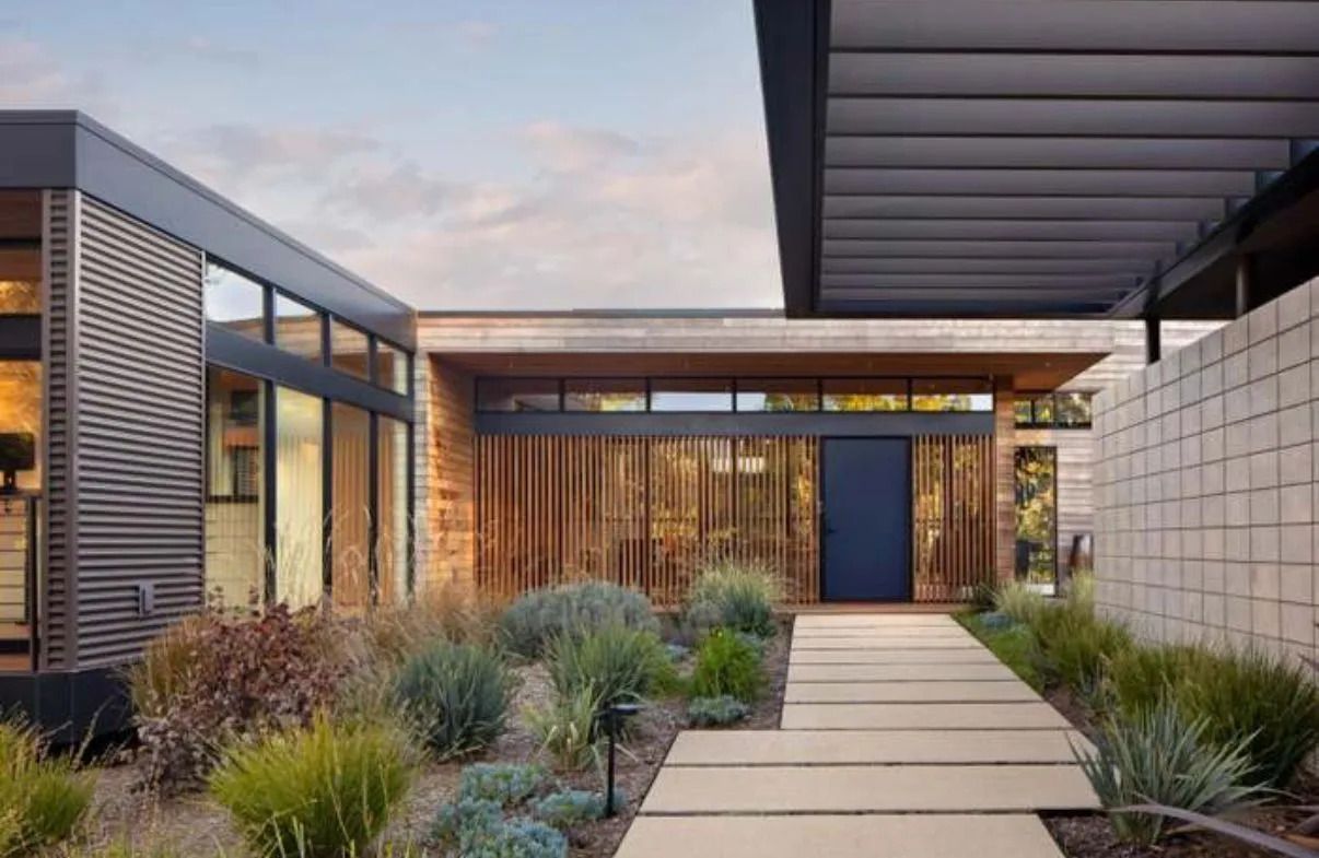 Modern home entrance with a wooden slat wall, a blue door, and a stone pathway.