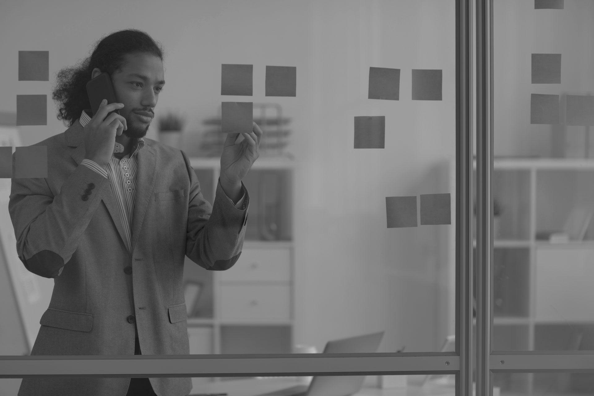 Man on phone looking at sticky notes on a glass wall in an office.