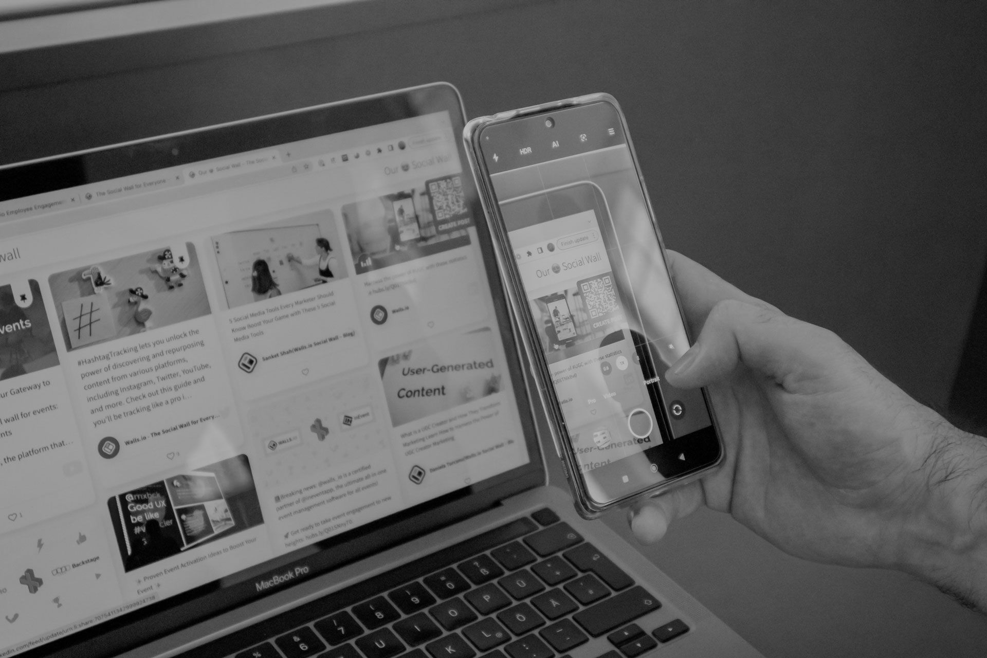 A person is holding a cell phone in front of a laptop computer.