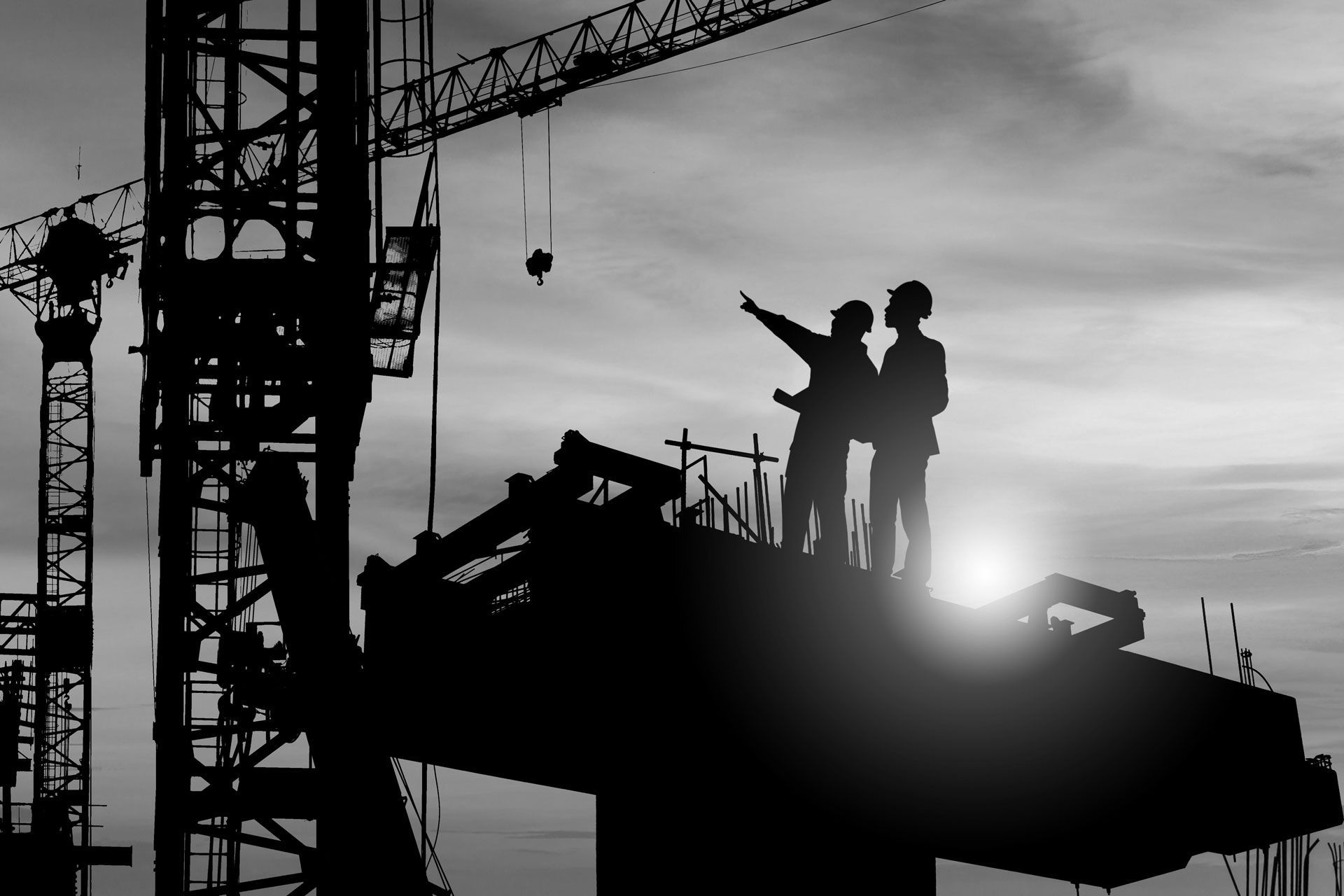 Two construction workers are standing on top of a building under construction