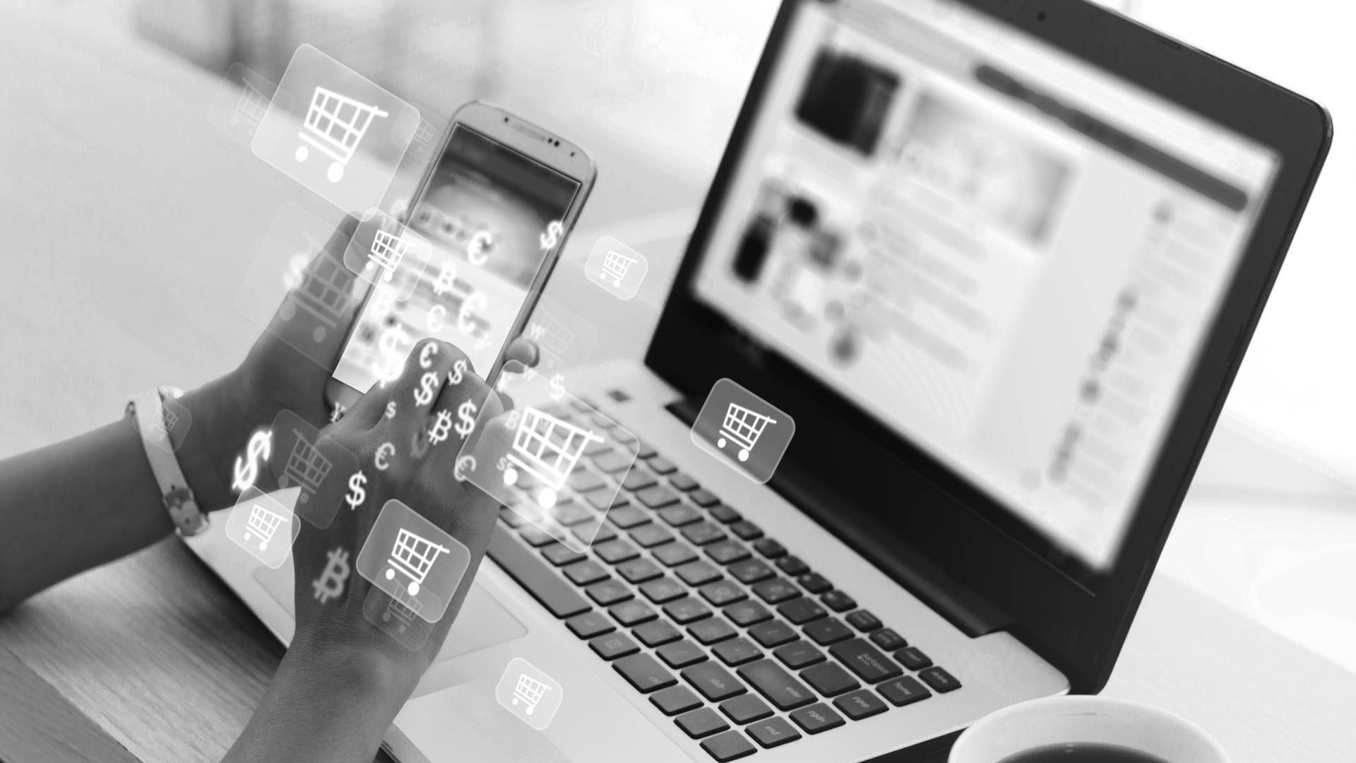 A person is holding a cell phone in front of a laptop computer.