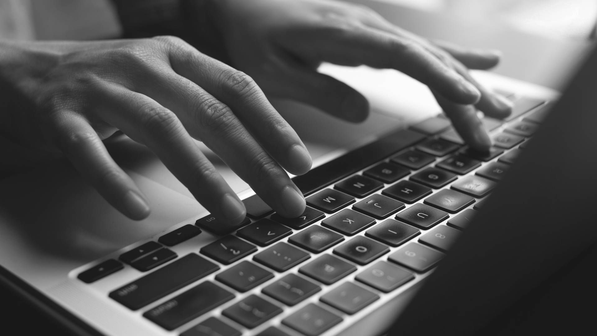 A person is typing on a laptop keyboard in a black and white photo.