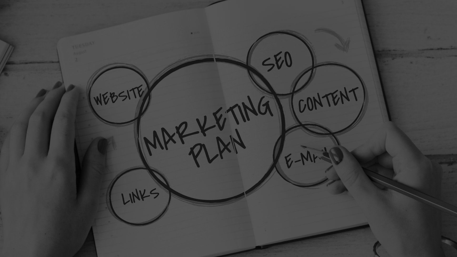 A person is writing a marketing plan in a notebook.