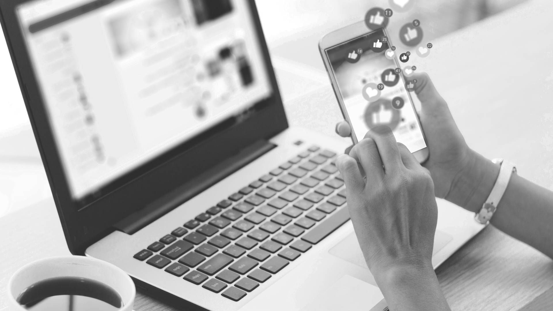 A person is using a cell phone in front of a laptop computer.