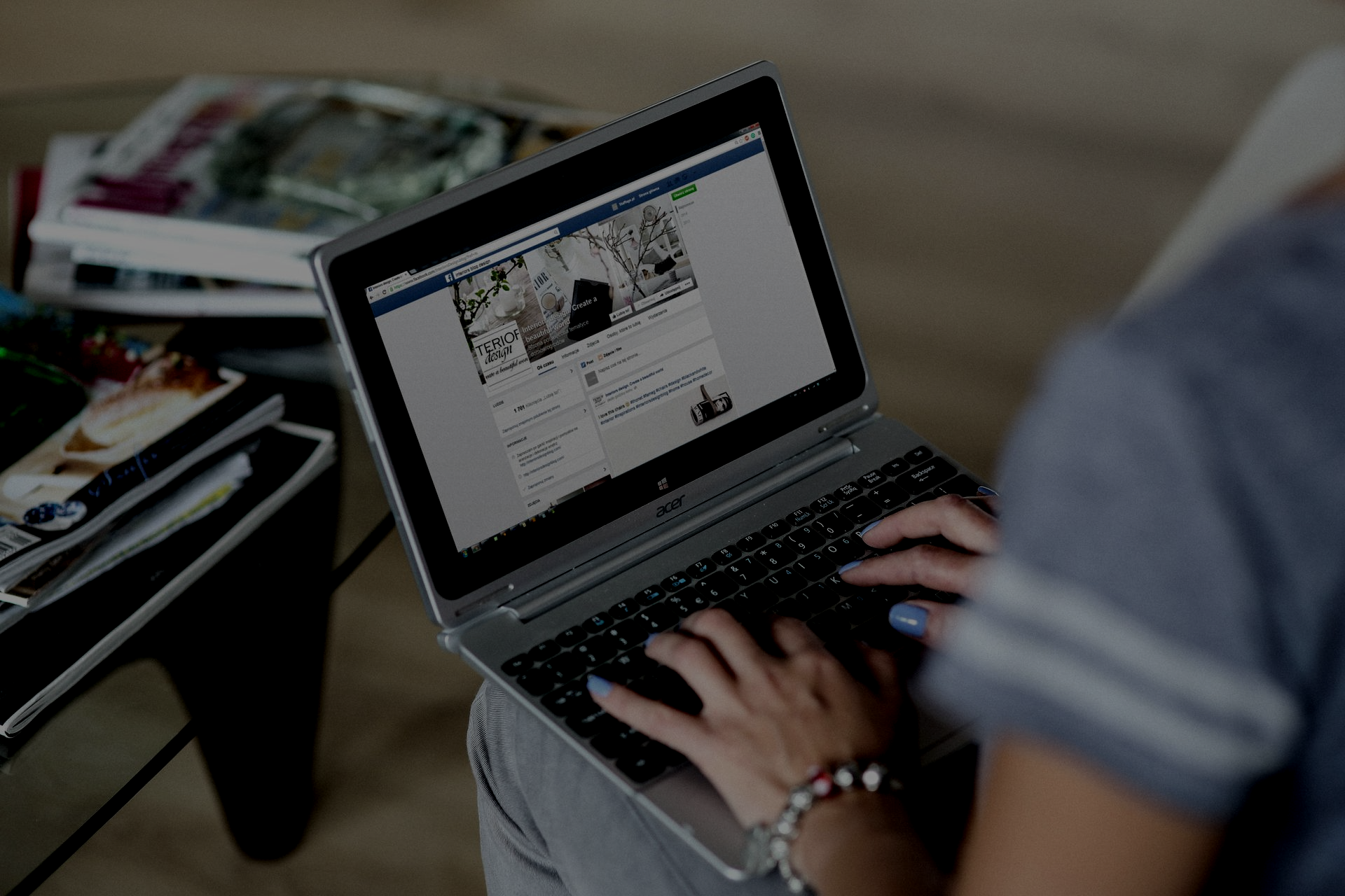 Person using a laptop, typing on keyboard, viewing Facebook feed.