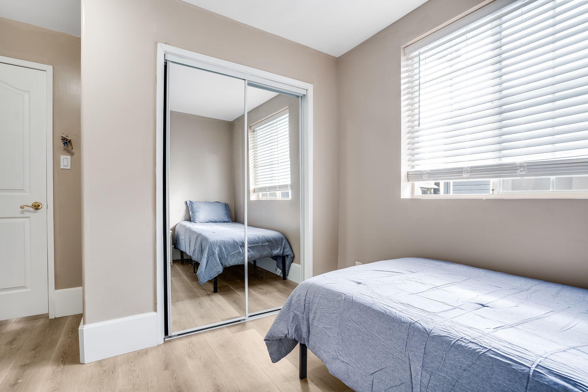 Bedroom with two twin beds and mirrored closet. Light walls, blinds, and wood-look flooring.