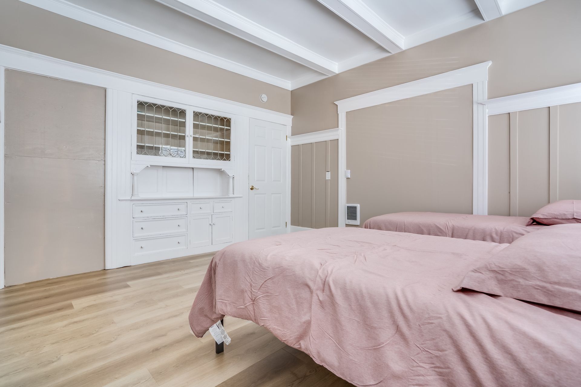 Bedroom with two beds, pale pink bedding, built-in white cabinet, and wood floors.