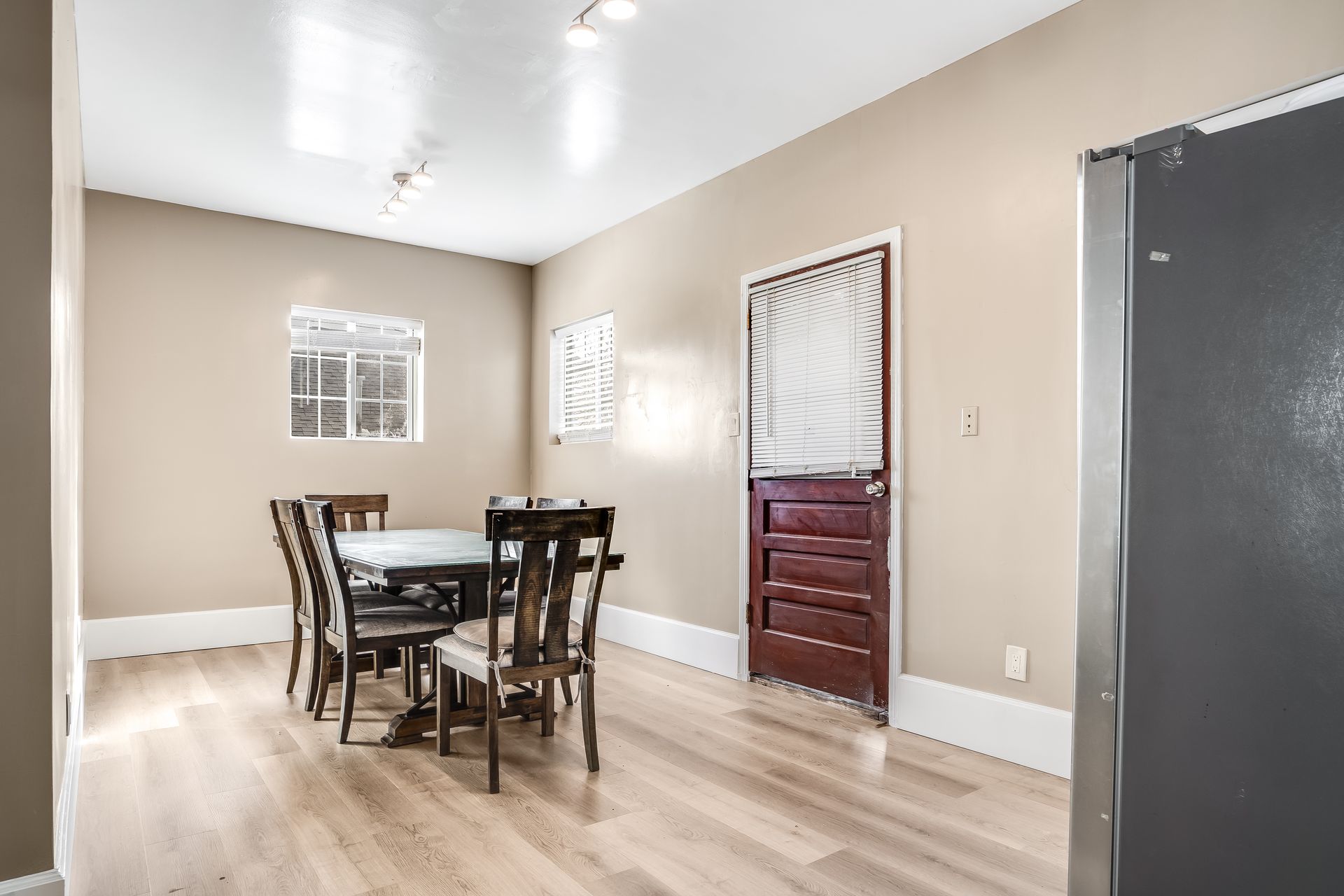 Dining room with a table, chairs, and a dark red door, light wood floor, beige walls.
