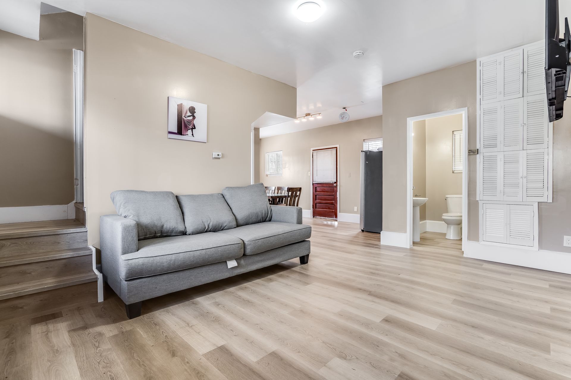 Living room with gray sofa, light wood floors, and open doorways.