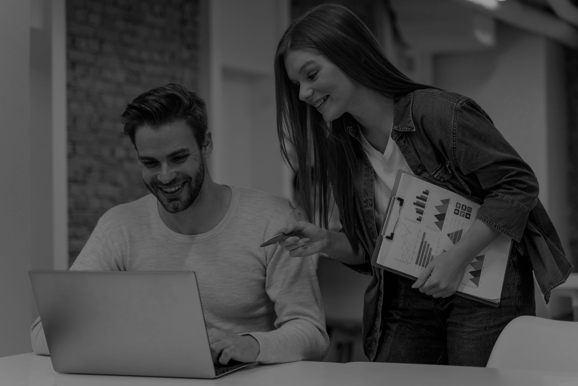 Man and woman looking at laptop, woman pointing at charts, smiling.