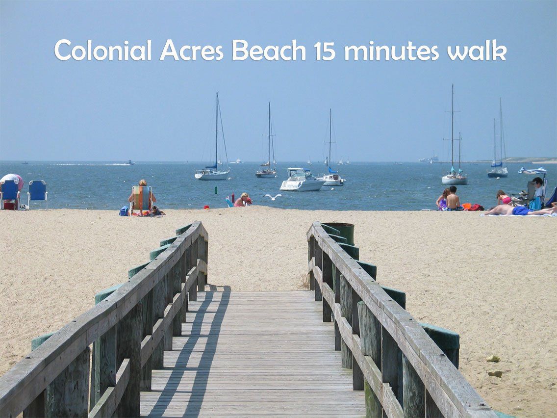Wooden boardwalk leading to a beach with sailboats in the water; text: Colonial Acres Beach 15 minutes walk.