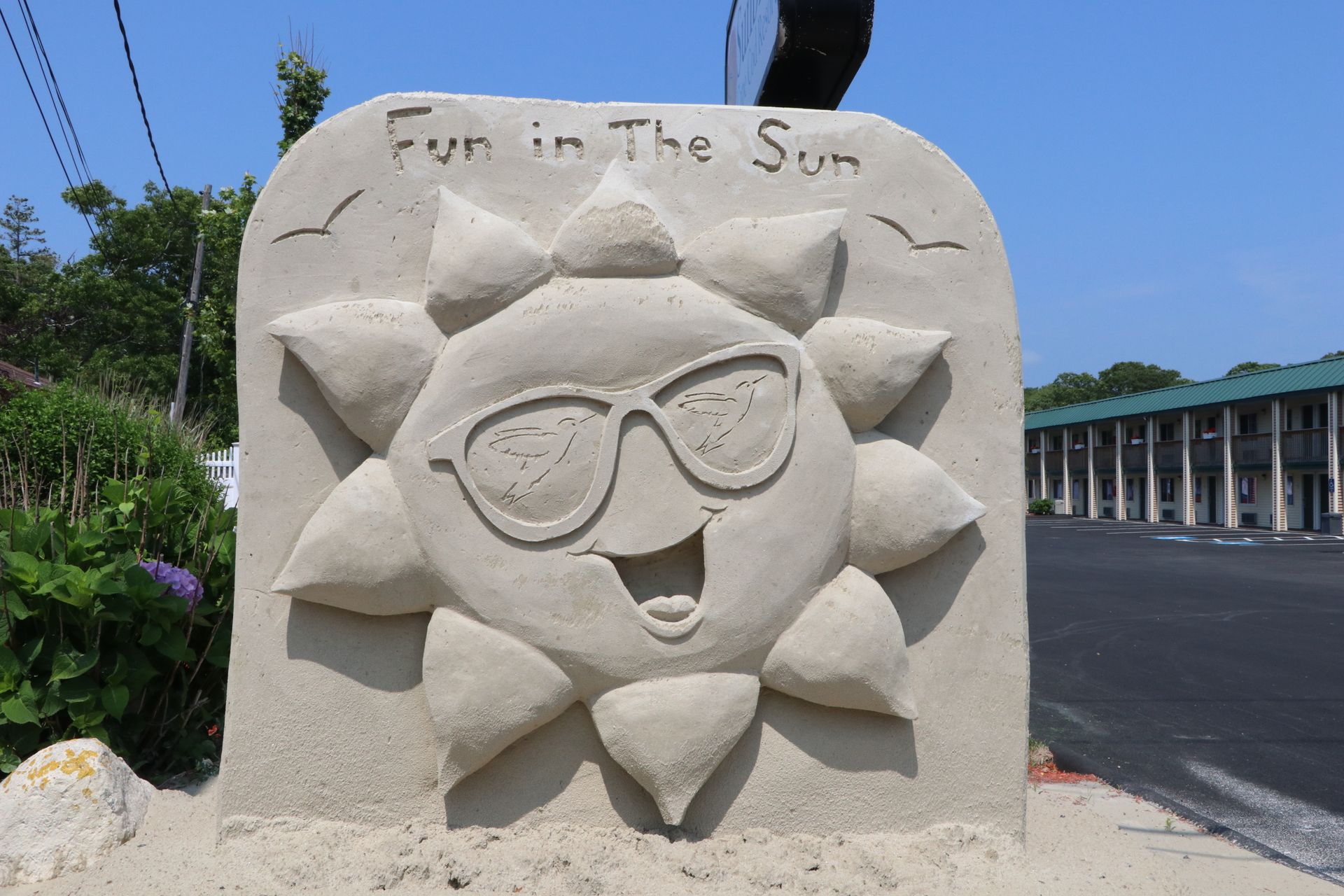 Sand sculpture of a smiling sun wearing sunglasses, with 