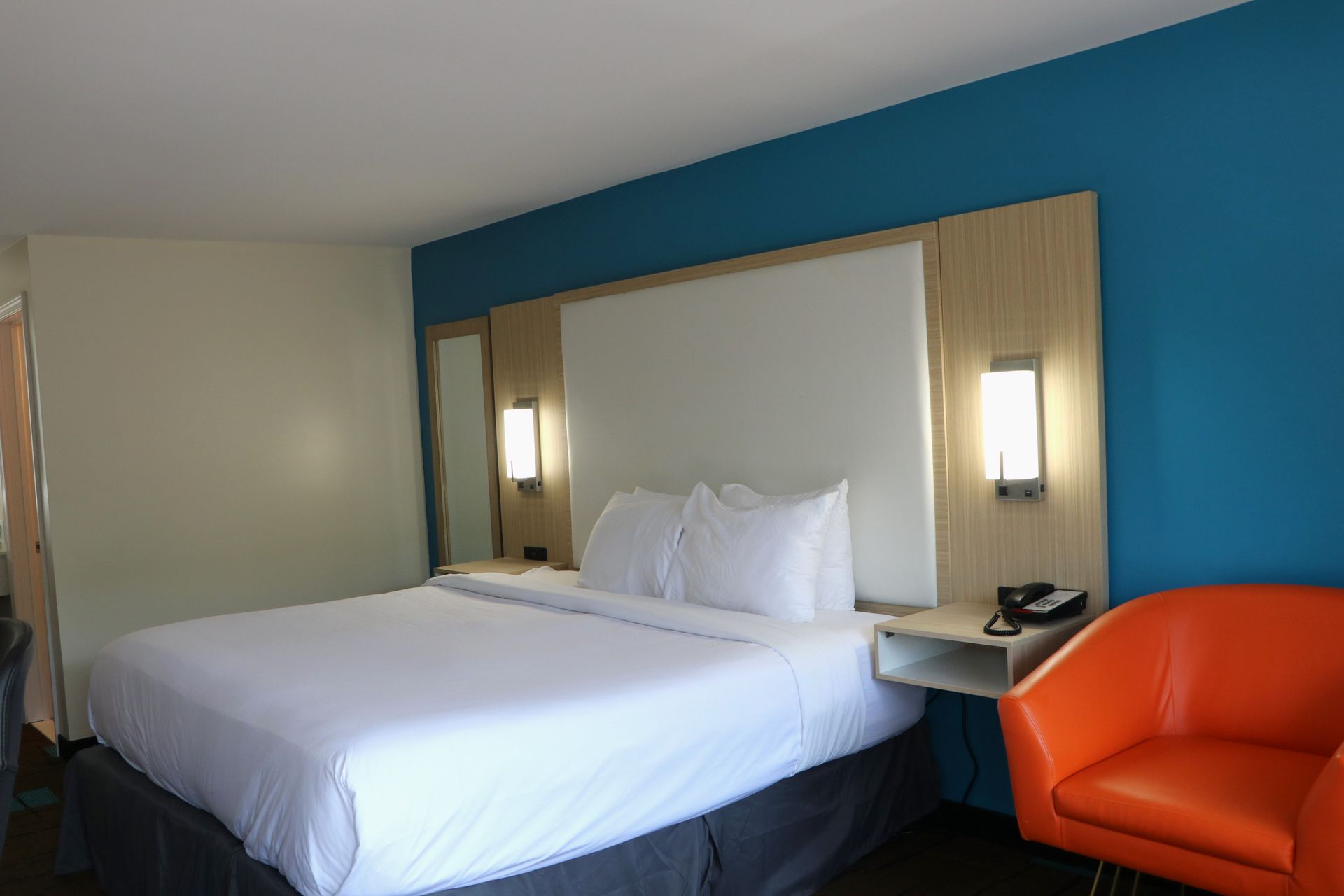 Hotel room with a bed, orange chair, and teal accent wall.