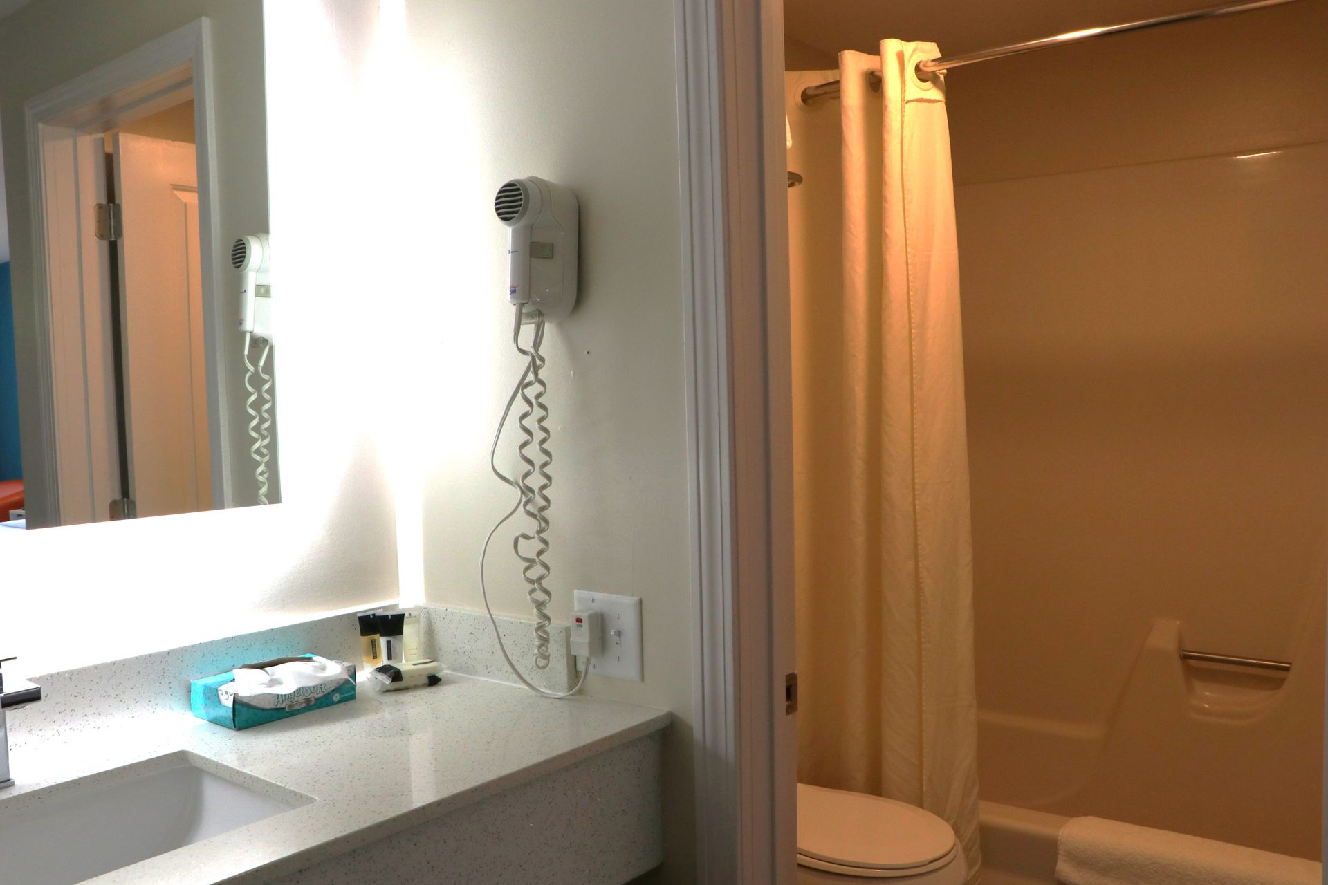 Bathroom with vanity, mirror, toilet, shower with curtain, and wall-mounted hairdryer.