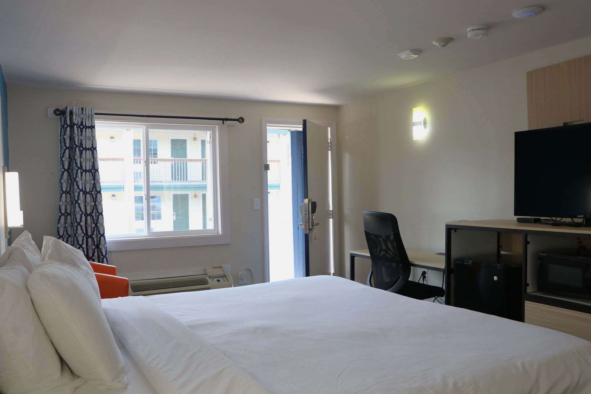 Hotel room with a bed, TV, desk, window, and door.