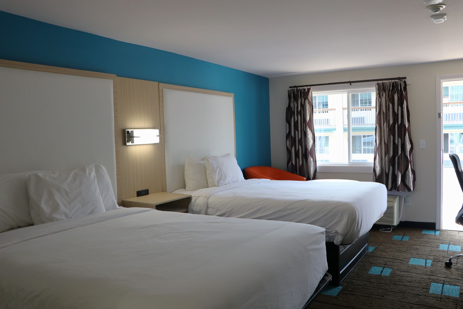 Hotel room with two beds, white bedding, turquoise wall, window with curtains, and patterned carpet.