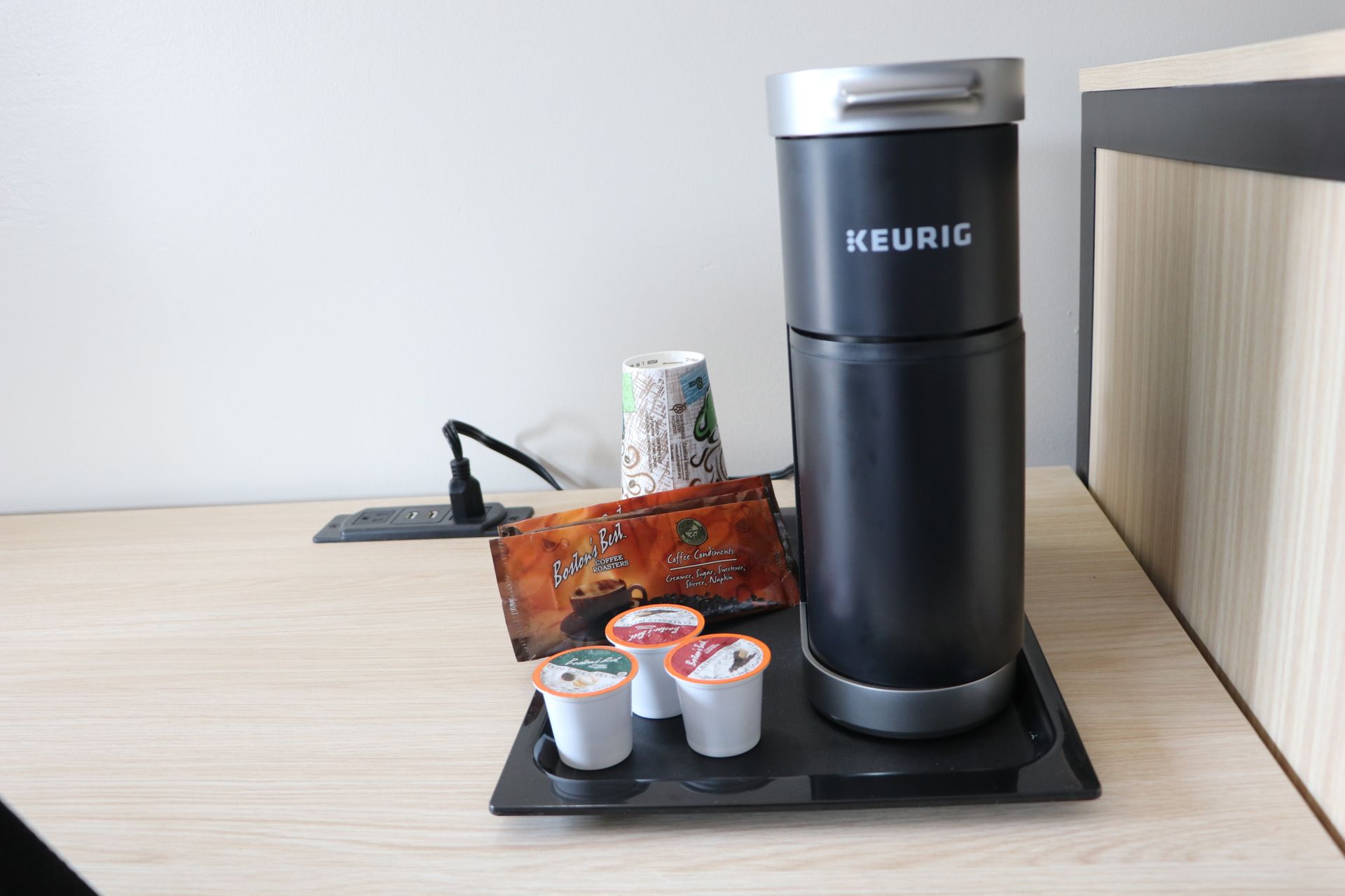 Keurig coffee maker with K-cups on a tray, on a light wood surface.