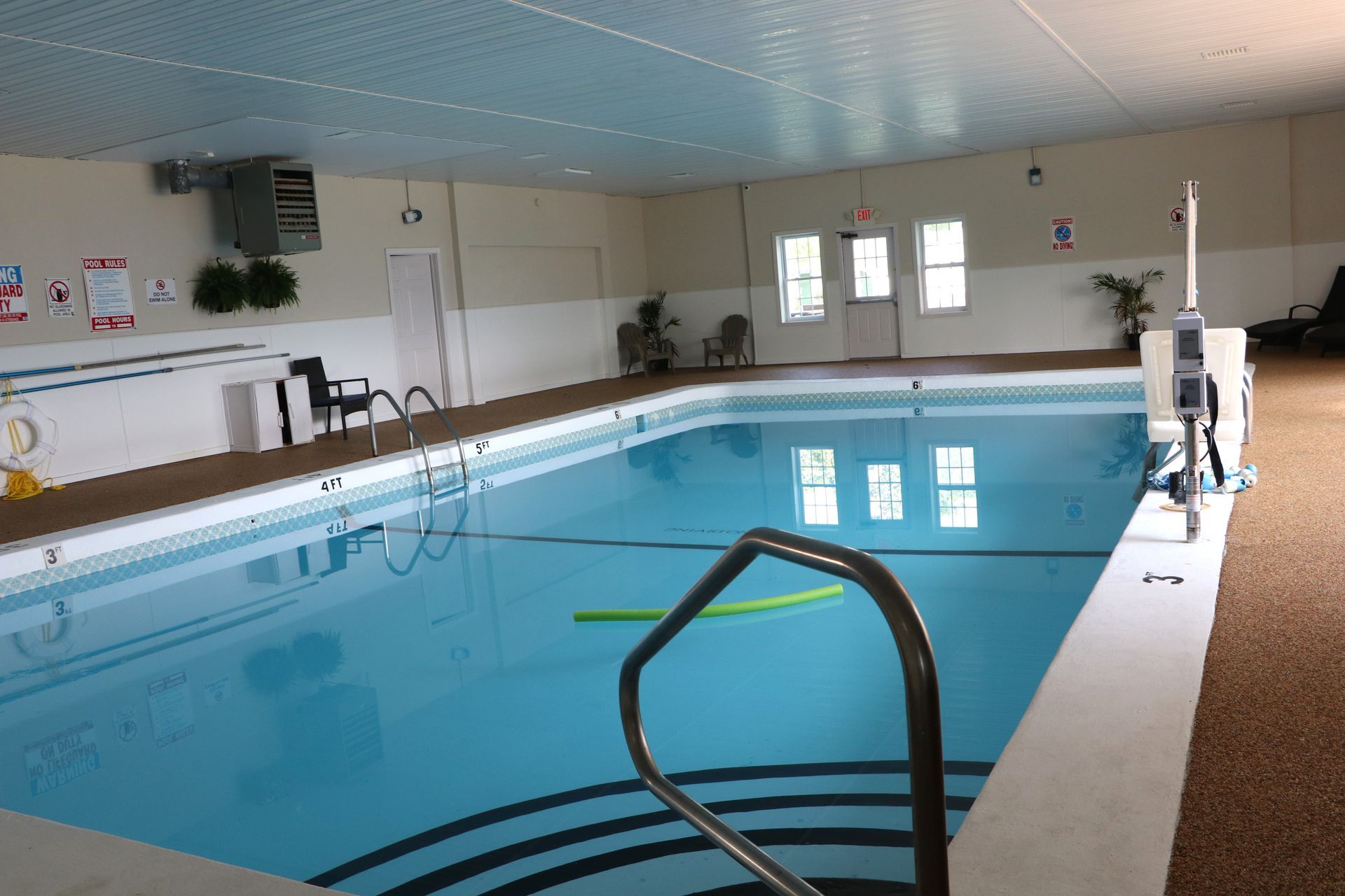 Indoor rectangular swimming pool with clear water, blue lane lines, and a metal handrail.