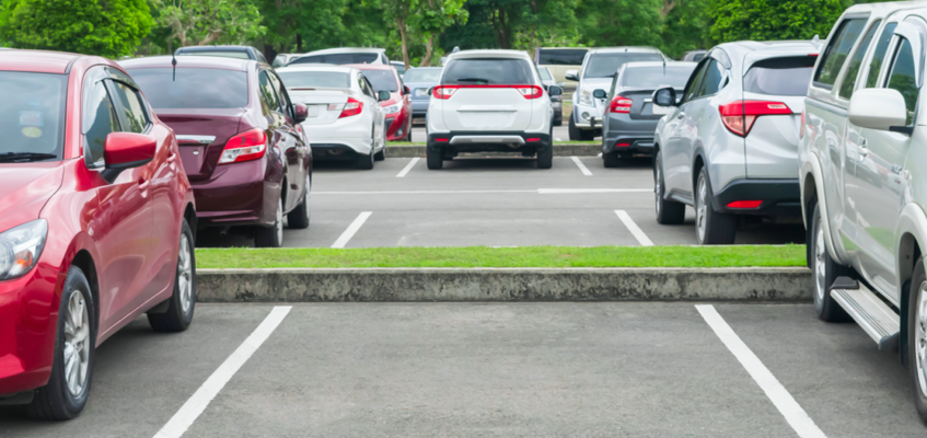 Cars parked in an asphalt parking lot, separated by white lines and a patch of grass.