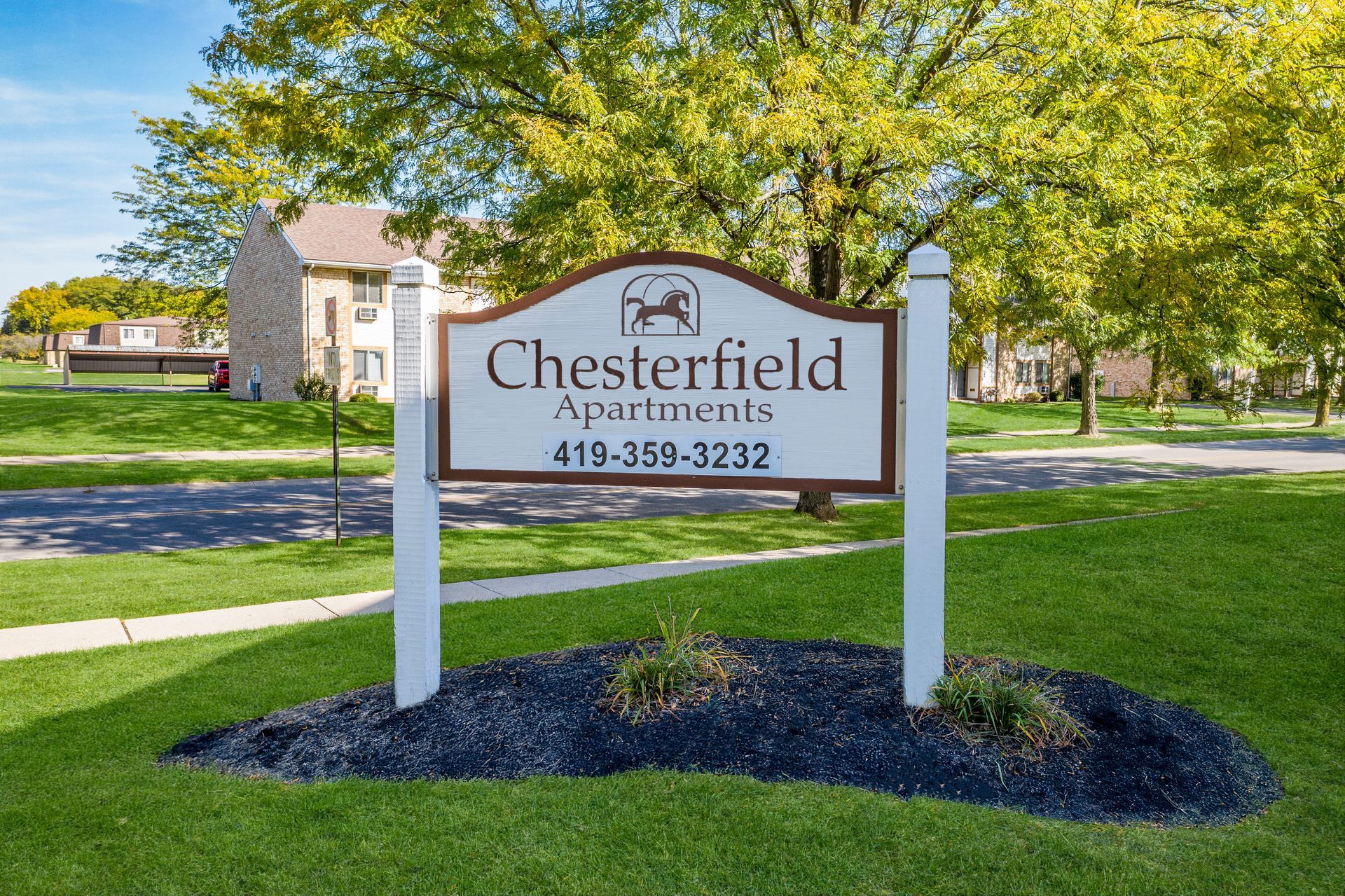 Photo of the sign for Chesterfield Apartments, with trees in the middle ground and the homes in the background