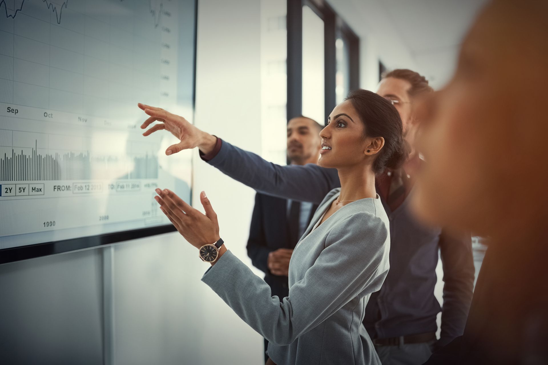 A woman is pointing at a screen while a group of people look on.
