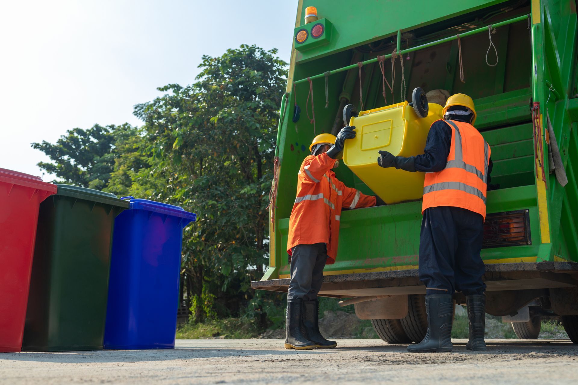 Two sanitation workers emptying a yellow recycling bin into a green garbage truck.