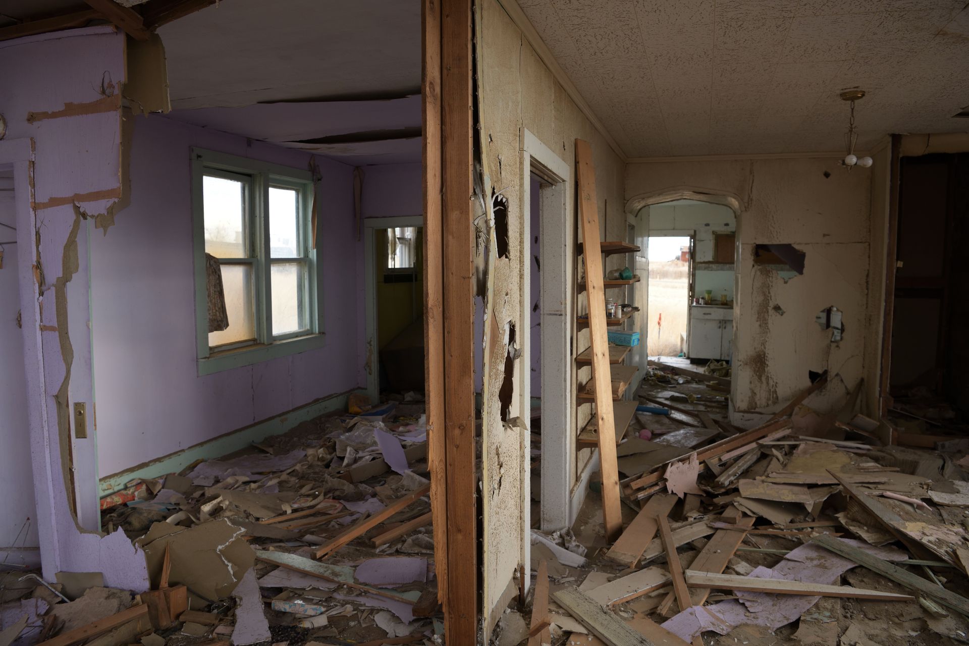Interior of a dilapidated room with debris, peeling paint, and visible structural damage.