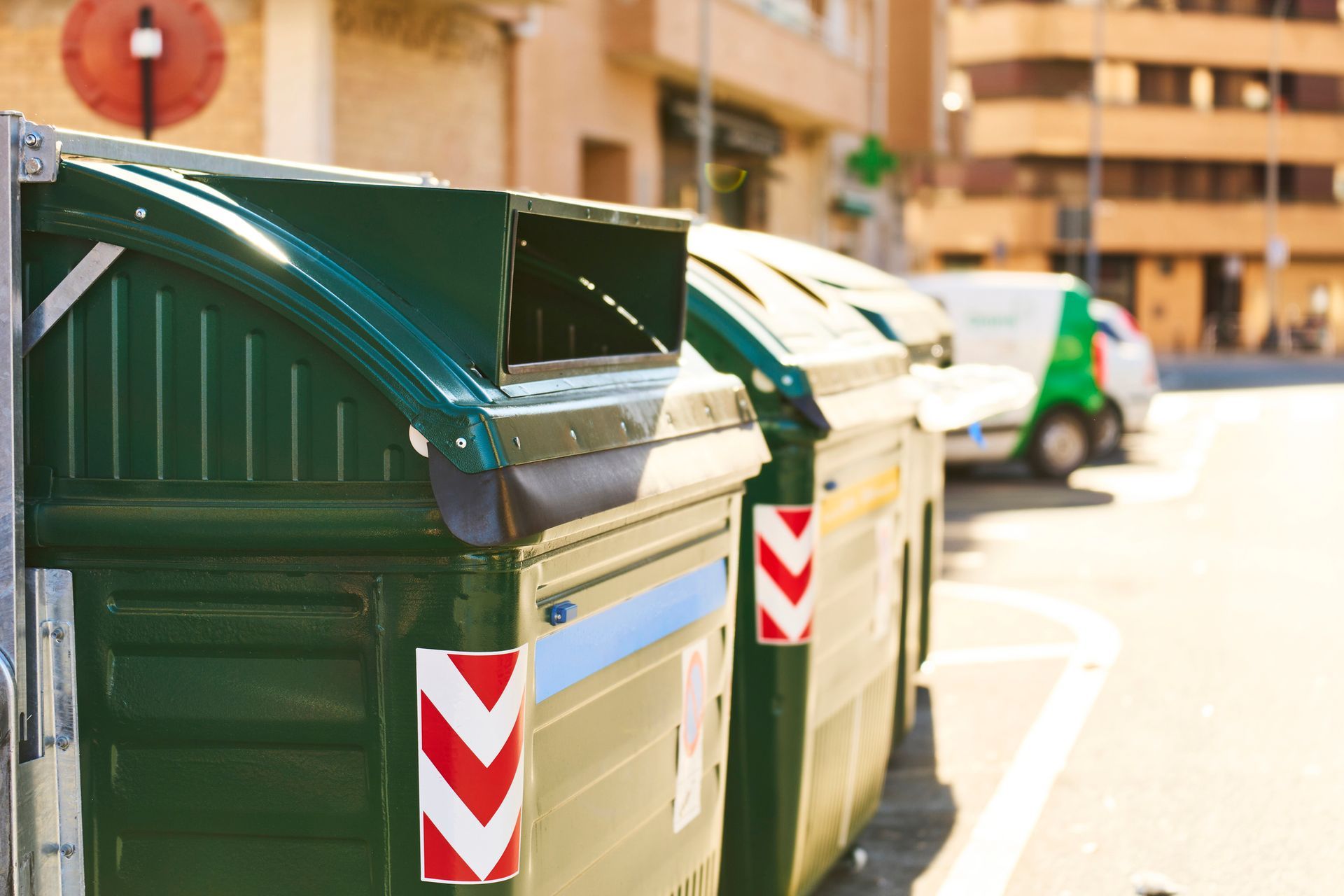 Green recycling bins on a city street with a blurred background of buildings and a van.