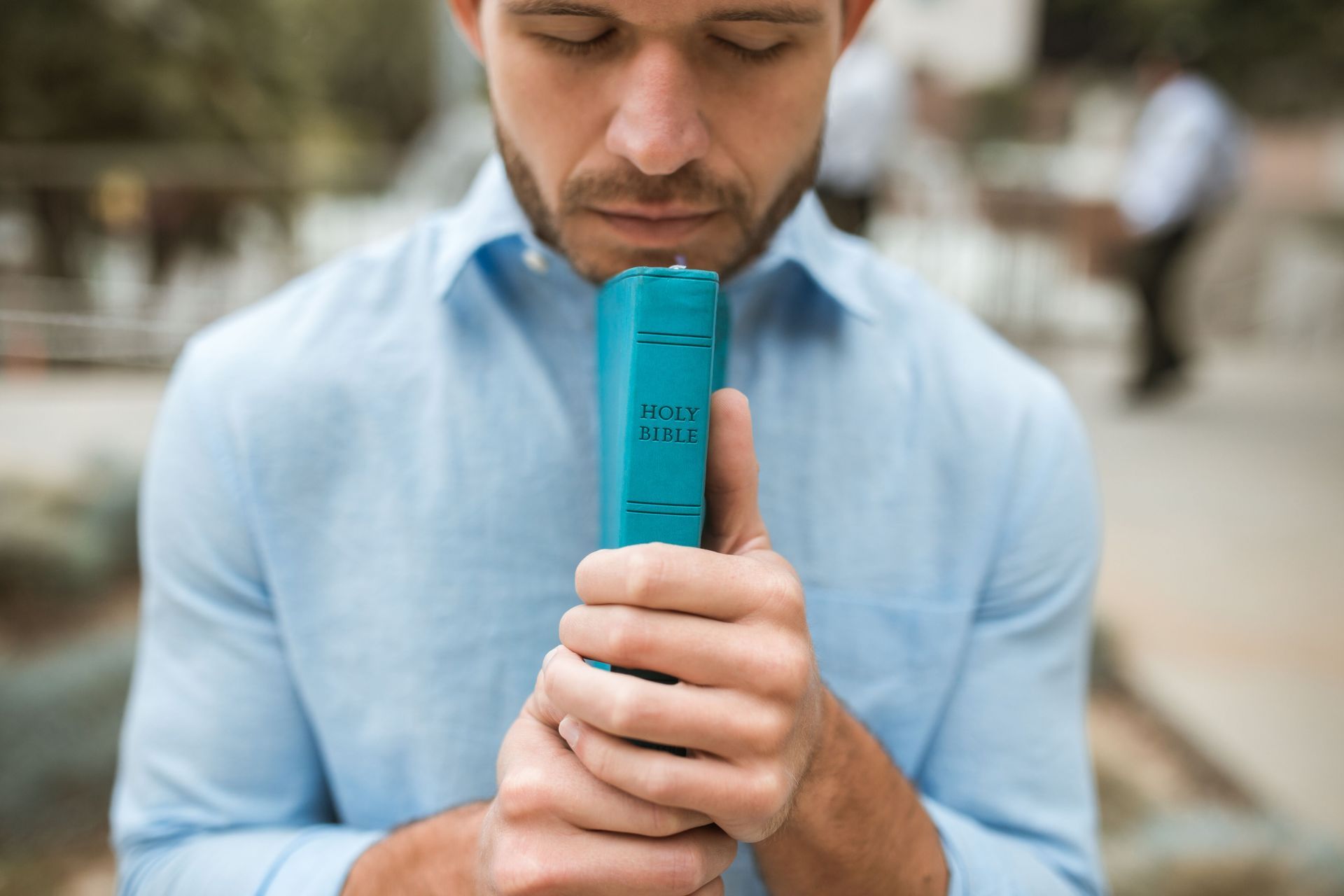 Man in light blue shirt holding a turquoise inhaler to his mouth outdoors