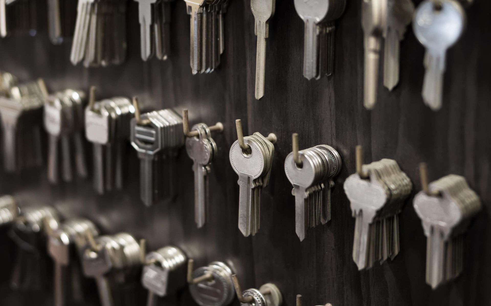 Rows of silver keys hanging on a dark wall display, neatly arranged in a key shop.