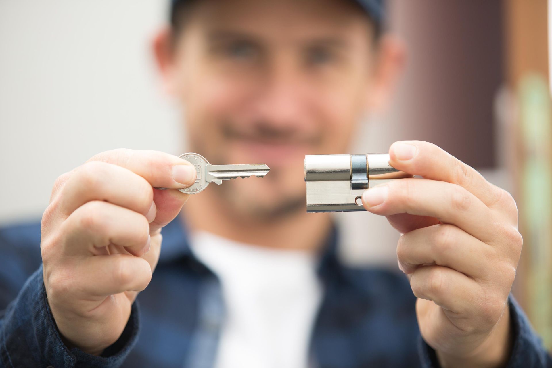 Person holding a key and a metal lock cylinder, with a blurred background outdoors.