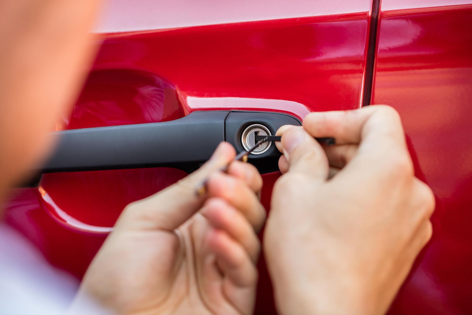 Hands using a key on a red car door lock