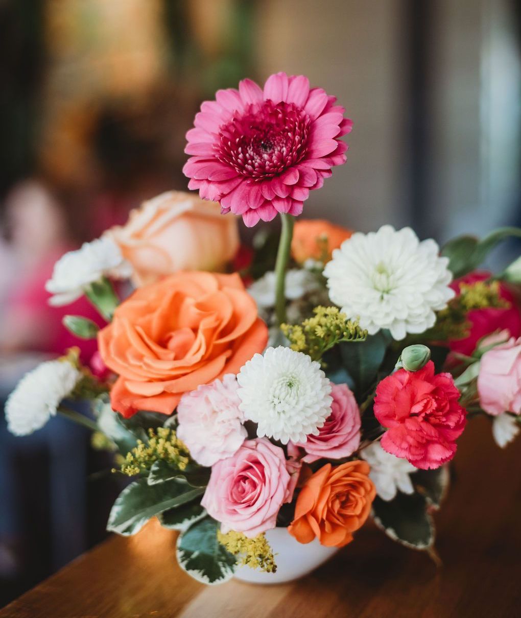 Close-up of a vibrant flower arrangement in a white bowl, featuring pink, orange, and white blooms.