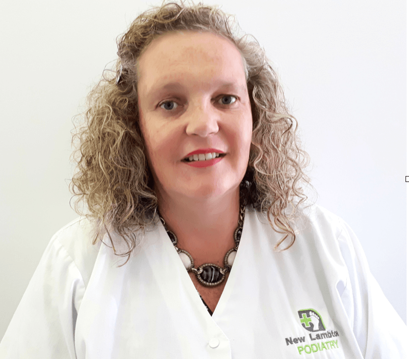 A woman with curly hair is wearing a white coat and a necklace.