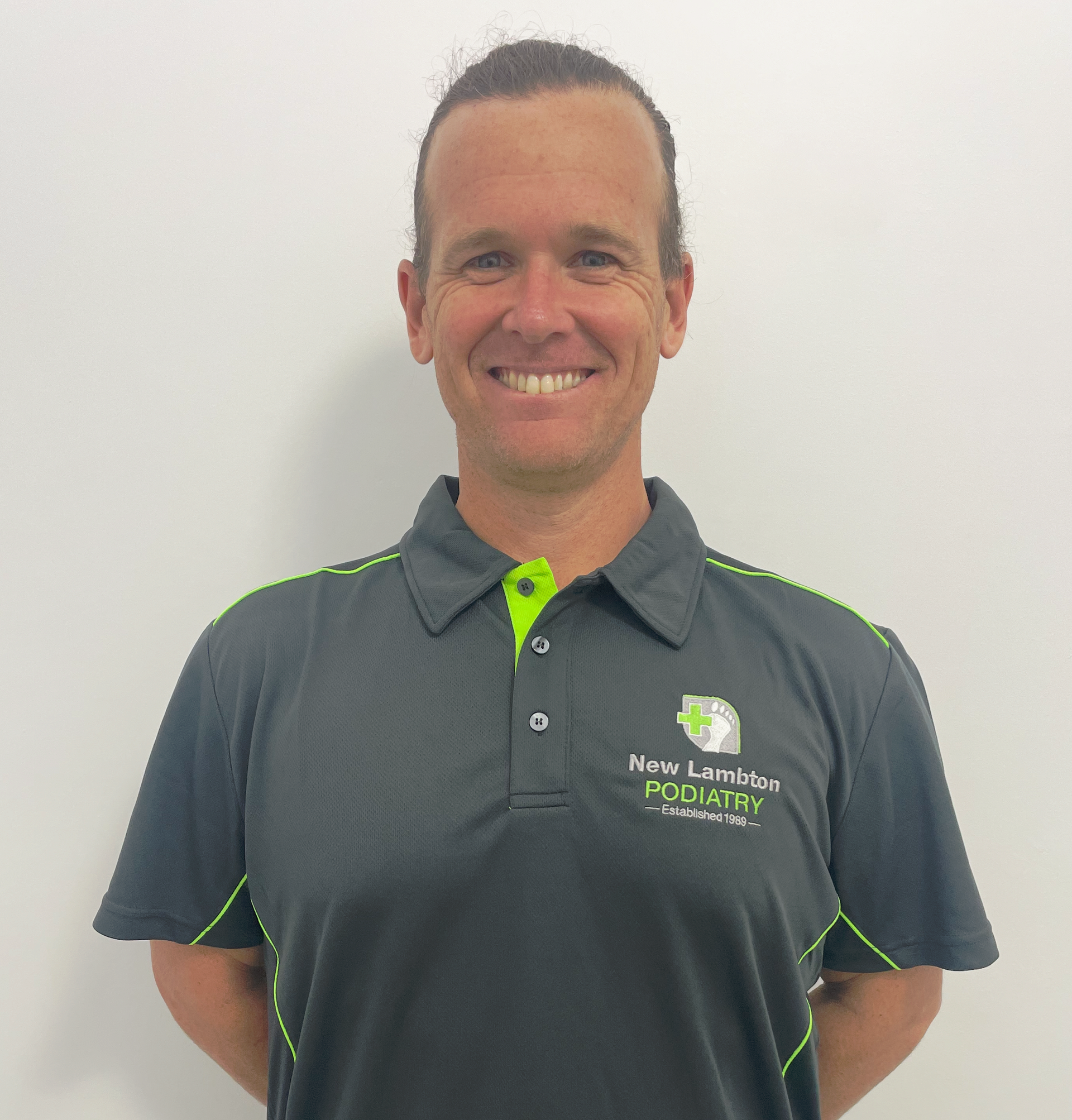 A man wearing a black and green polo shirt is smiling for the camera.