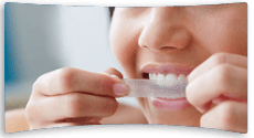Woman applying a strip to her teeth to make her teeth look whiter