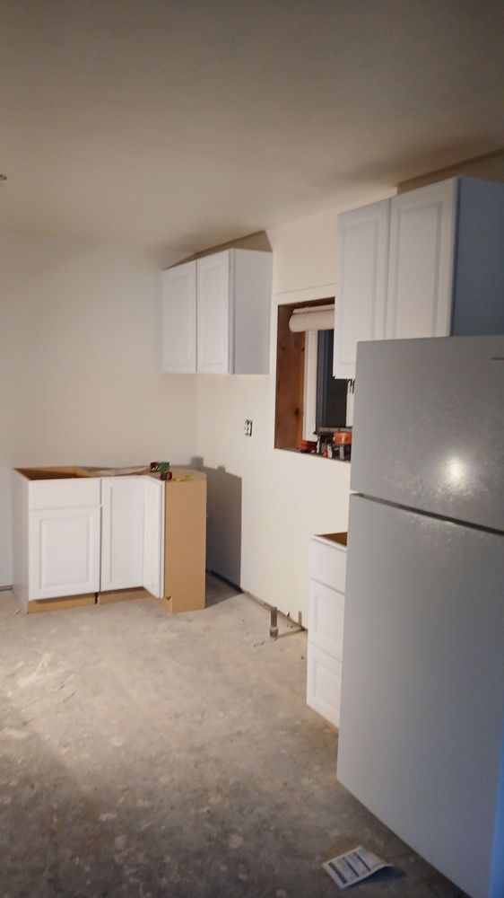 Unfinished kitchen with white cabinets, refrigerator, and bare floor under renovation
