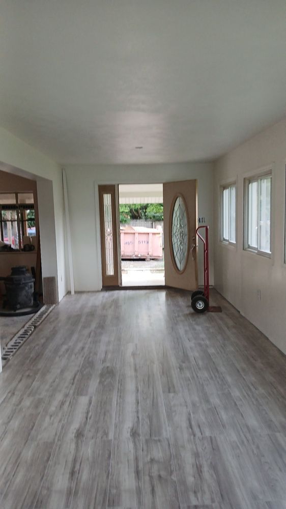 Empty living room with gray wood floors, white walls, and a front door opening to a patio.