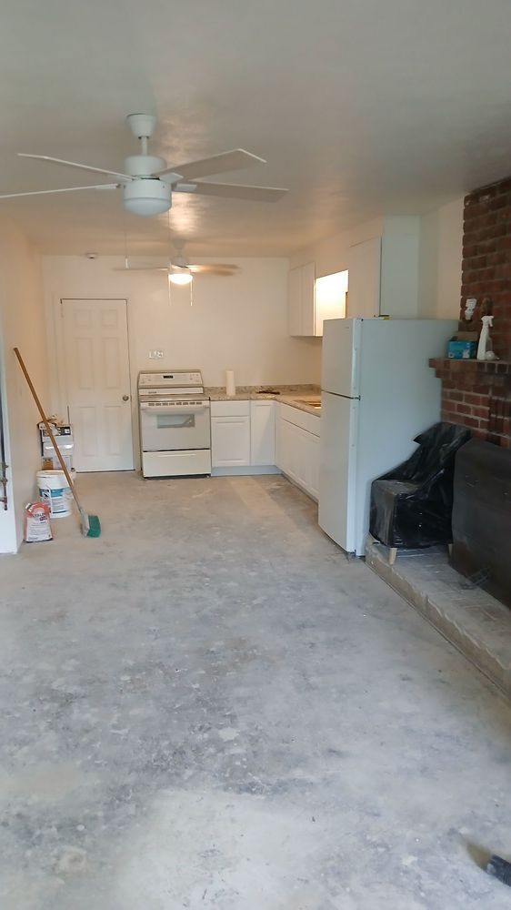Empty garage with ceiling fan, stove, white cabinets, refrigerator, and fireplace along one wall