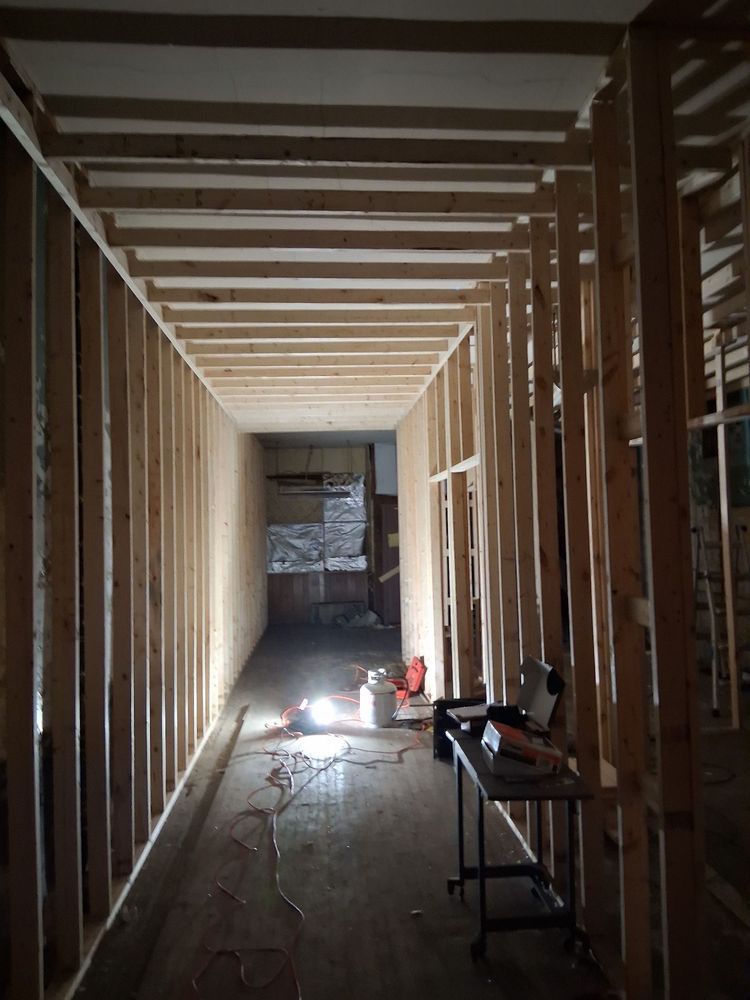 Framed hallway under construction with exposed wood studs, workbench, and tools on the floor.
