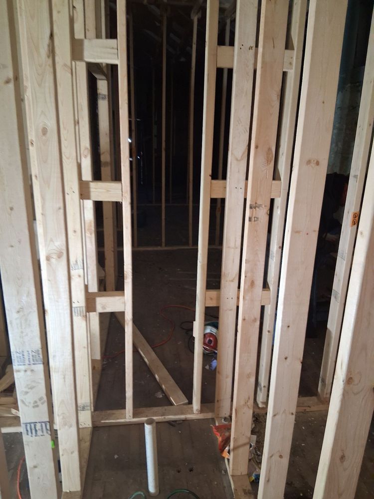 Unfinished interior wall framing with open doorway and exposed wooden studs in a narrow hallway.