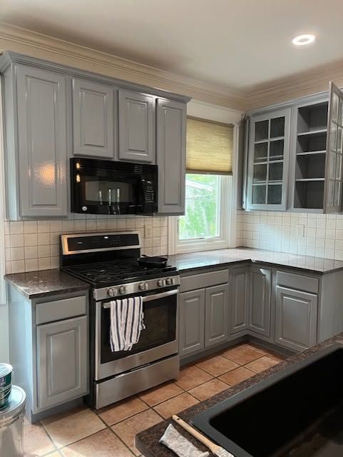 Gray kitchen with black countertops, stainless stove, and window over the sink
