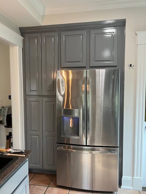 Stainless steel refrigerator framed by dark gray kitchen cabinets in a bright kitchen