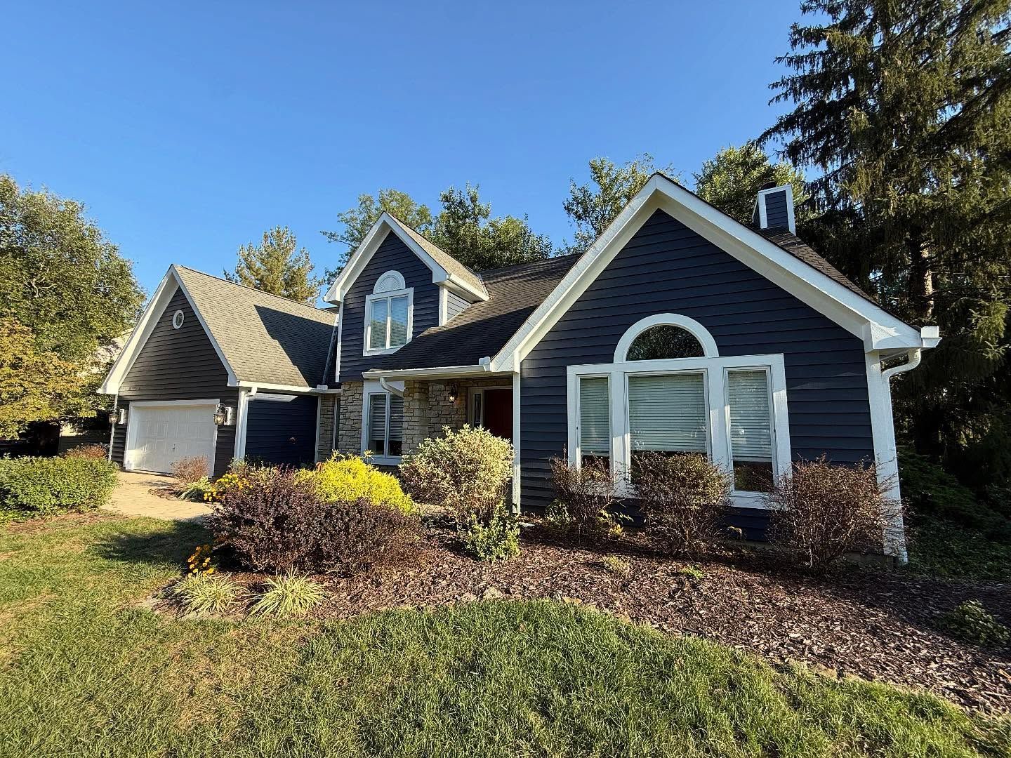 Suburban house with gray siding, white trim, and a landscaped front yard in sunlight