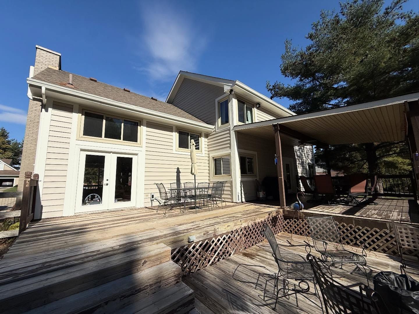Two-story beige house with a wooden deck and covered patio under a blue sky