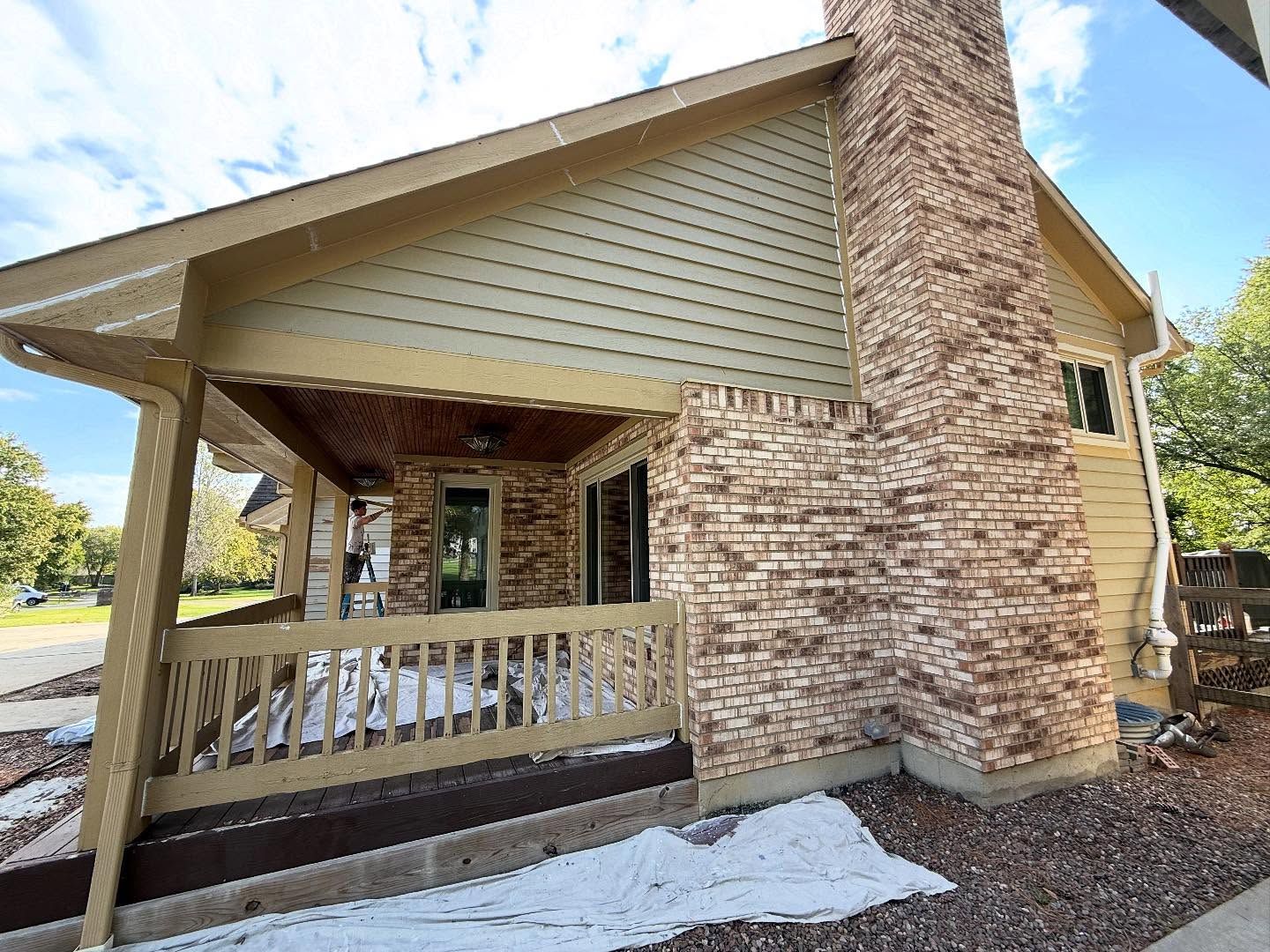 Covered porch with wooden railing and stone columns on a house exterior, with snow on the ground