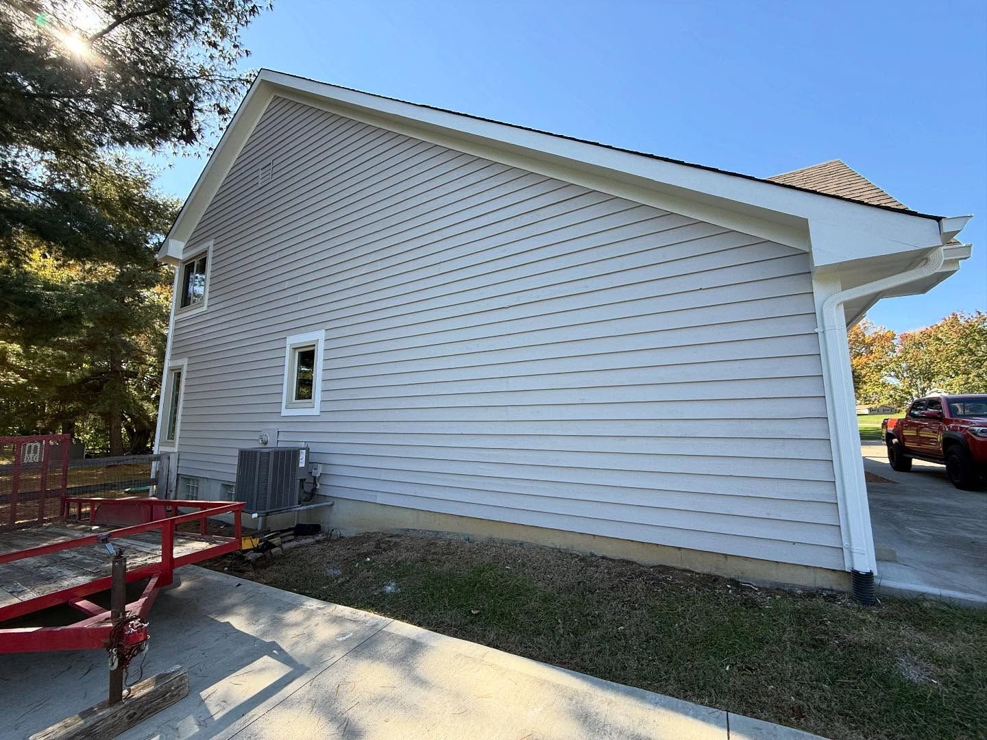 White house exterior with gray siding, small windows, and a red trailer in the driveway.