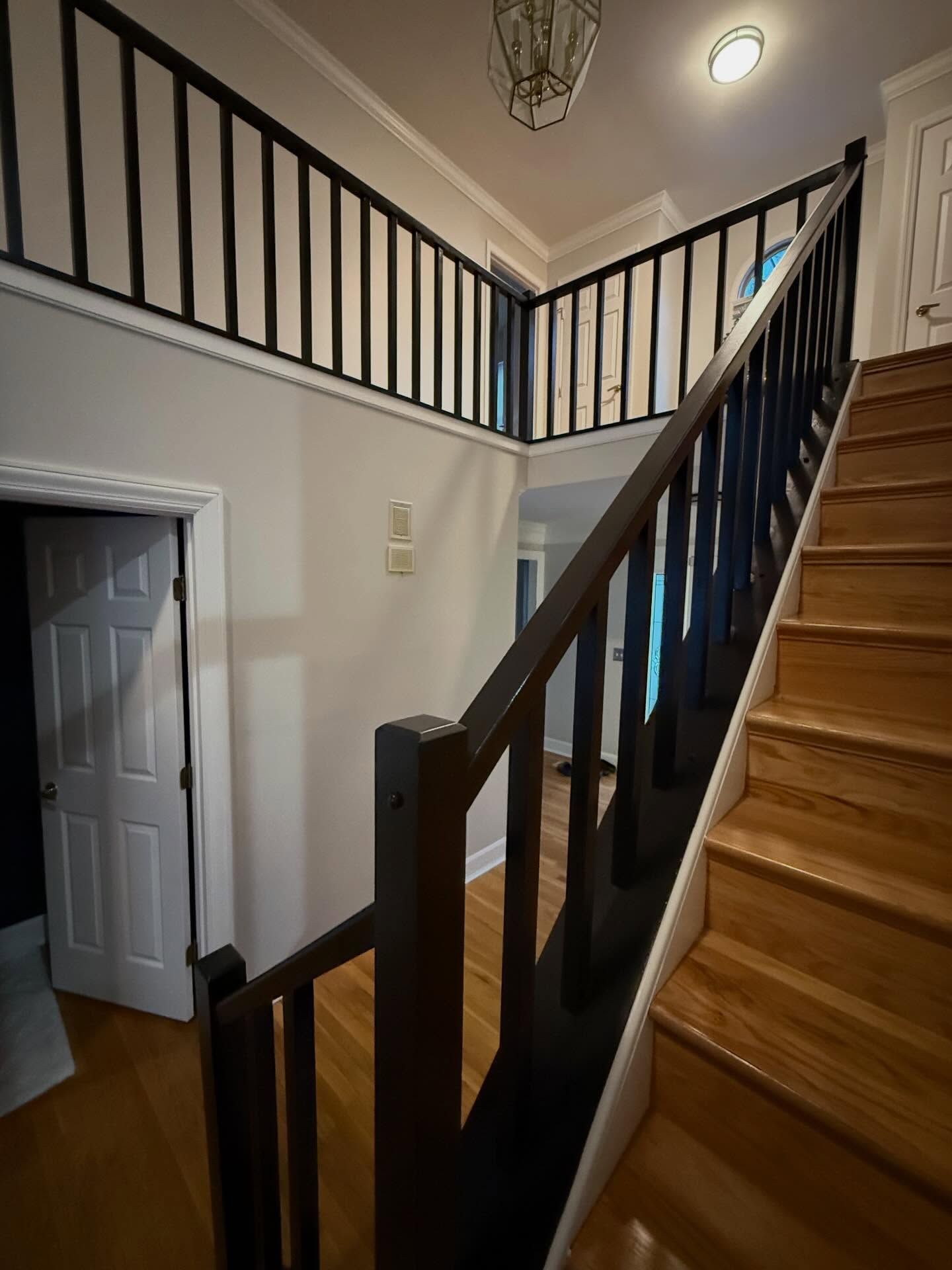 Staircase with wooden steps, black railing, and a hallway below with an open door.