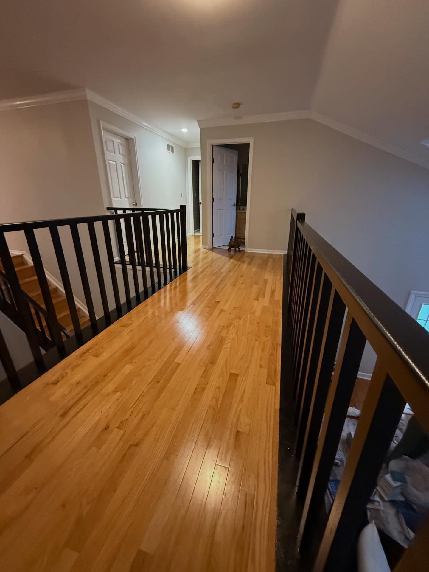 Upstairs hallway with hardwood floors, black railings, and sloped white ceiling leading to a doorway