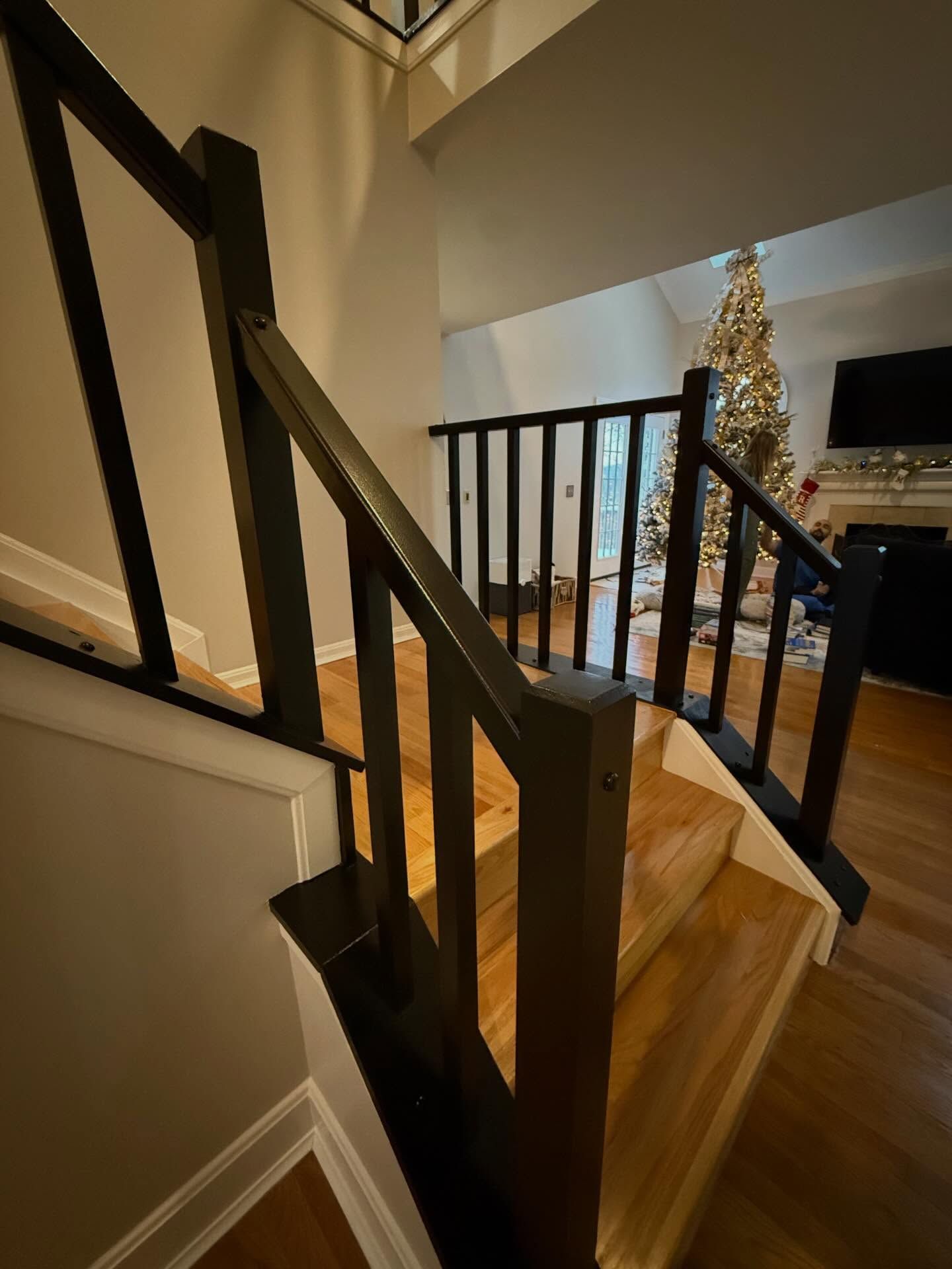 Staircase with dark railing, wooden steps, and a lit Christmas tree in the background.